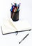 Black pen, open small unfold notebook, note with blank empty light pages near metallic glass stationery with pens and felt pens