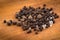 Black peppercorns and Allspice on a wooden background.