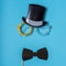 Black photo booth props: cylinder hat, glasses and bow tie on blue background. Greeting card for father`s day. Creative