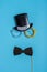 Black photo booth props: cylinder hat, glasses and bow tie on blue background. Greeting card for father`s day. Creative