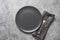 Black plate, fork and knife on grey stone table. Elegance table place setting. Copy space. View from above.