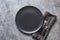 Black plate, fork and knife on grey stone table. Minimal table place setting. Space for text or menu. View from above