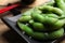 Black plate with green edamame beans in pods on wooden table, closeup