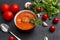 Black plate of red tomato soup with meat meatballs, cilantro on a black,   spoon, cloves and head of garlic, fresh tomatoes