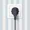 Black plug inserted in a wall socket on backdrop of wall with wallpaper