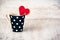 Black polka dotted coffee cup with a heart shaped homemade cookie over white wood background.