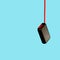 Black powerbank hangs on red USB charging wire on blue background