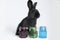 A black rabbit on a white background. Colorful little jars