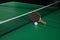 Black racket and ball on green ping pong table indoors