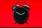 Black realistic alarm clock isolated on red background. 3d rendering.