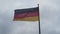 Black, red and gold colour. Close up of German national flag on pole waving in wind against overcast sky.