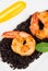 Black rice risotto with shrimp and safron sauce in a white plate seen from above in white background close