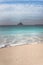 Black rock on ocean horizon. Defocused ocean wave rolling to sandy beach with clear transparent azure water. White