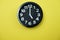 Black round clock showing five o`clock on yellow background