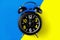 Black round metal alarm clock on legs on a bright composite background of blue and yellow color.