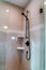 Black round shower head on tile wall of shower stall with hinged glass door