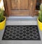 Black Rubber Ellipse Design Eyes Floor Door Mat outside home with yellow flowers and leaves