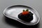 Black salty caviar of sterlet decorated with red salmon caviar and mint leaves on black ceramic plate of unusual shape on black