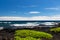 Black Sand beach on the Big Island of Hawaii; black volcanic rock and vegetation in foreground, blue ocean and waves in background