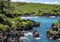Black sand beach surrounded by luxurious tropical vegetation and rugged shoreline with lava rocks on the Island of Maui.