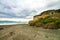 Black sand wild beach in Catlins with primitive coastal wooden beach house in the cliff rocks, wind shaped trees, Gemstone beach