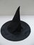 Black satin peaked witch hat on a gray and white backdrop with copy space.