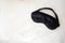 Black satin-silk sleep mask on white bed linen background, no people. Copy space. Comfortable relaxing sleep concept