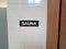 Black sauna sign on white tiled wall with sauna room to the right