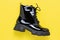 Black short boot on a yellow background. Patent leather shoes. Autumn women`s lace-up shoe. Modern outdoor boots on tractor sole.