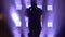 Black silhouette against the background of purple spotlights in a dark studio. Young energetic guy dancing hip hop