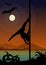 Black silhouette of female pole dancer performing pole moves in front of river and full moon at Halloween night