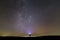 Black silhouette of man with head flashlight on grassy field under beautiful dark summer starry sky.