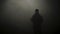 Black silhouette of man standing in smoky dark. Stock footage. Mysterious silhouette of young man stands in darkness lit