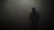 Black silhouette of man standing in smoky dark. Stock footage. Mysterious silhouette of young man stands in darkness lit