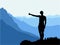 Black silhouette of man standing on the top of the hill, thumb up, enjoying beautiful view. Mountains in the background.