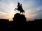 Black silhouette of monument of horse rider on background of rose sunset