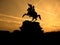 Black silhouette of monument of horse rider on background of yellow sunset