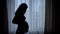 Black silhouette of nice pregnant woman stroking her belly standing near window