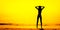 Black silhouette of slim girl on the sea beach, hands by head, yellow tone