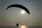 Black silhouette of a tandem of paragliders on a parachute flying over the evening ocean with a sun path during sunset