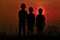 Black silhouette of three children standing together. There is a sky at sunset