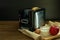 Black and silver electric micro oven with toast, fresh eggs, red apple and glass of milk on brown wooden and black background,