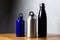 Black, silver and ultramarine thermo bottles on wooden table.