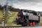Black single steam locomotive with red wheels. Water pump filling