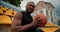 A Black-skinned athlete in a sports summer uniform sits on the stands of a yellow stadium, hits a basketball ball on the