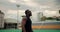 A Black-skinned man in a black sports uniform walks through the city stadium and rests looking back against the gray sky