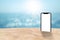 Black smartphone with blank white screen on sand beach with blurry seascape view and bokeh sunlight in background.