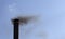 Black smoke billows from a black iron pipe against the sky