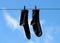 Black socks hang drying on the clothesline with clothespins. Closeup. On the background of blue sky with white clouds