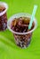 black sparkling cola water with bubbles in plastic cup with stroll on green table background feel thirsty